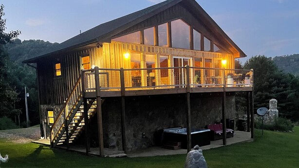 Une cabane en bois dotée d’un balcon, d’une cheminée en pierre et d’une cour gazonnée.