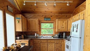 Une cuisine de style rustique, avec des éléments en bois, comprenant un coin repas, un revêtement de sol en carrelage de pierre et une fenêtre donnant sur un paysage verdoyant.