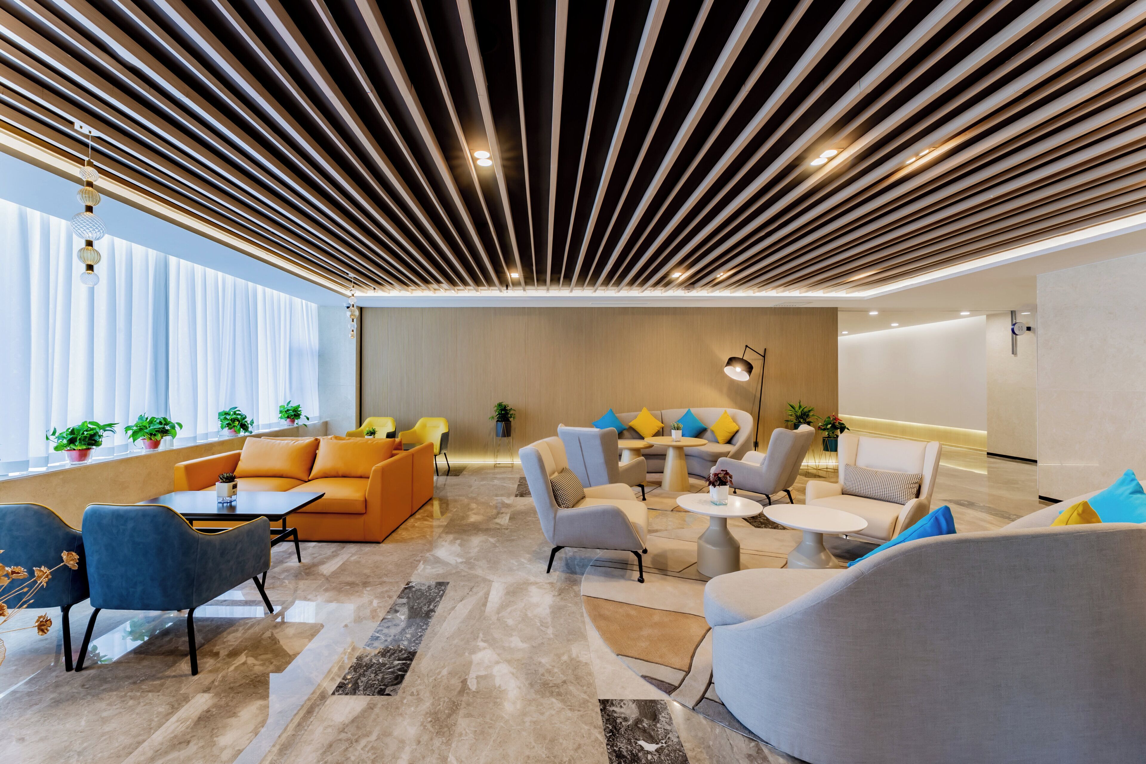 A modern lounge area with sofas, armchairs, and a coffee table, featuring a slatted ceiling and potted plants.
