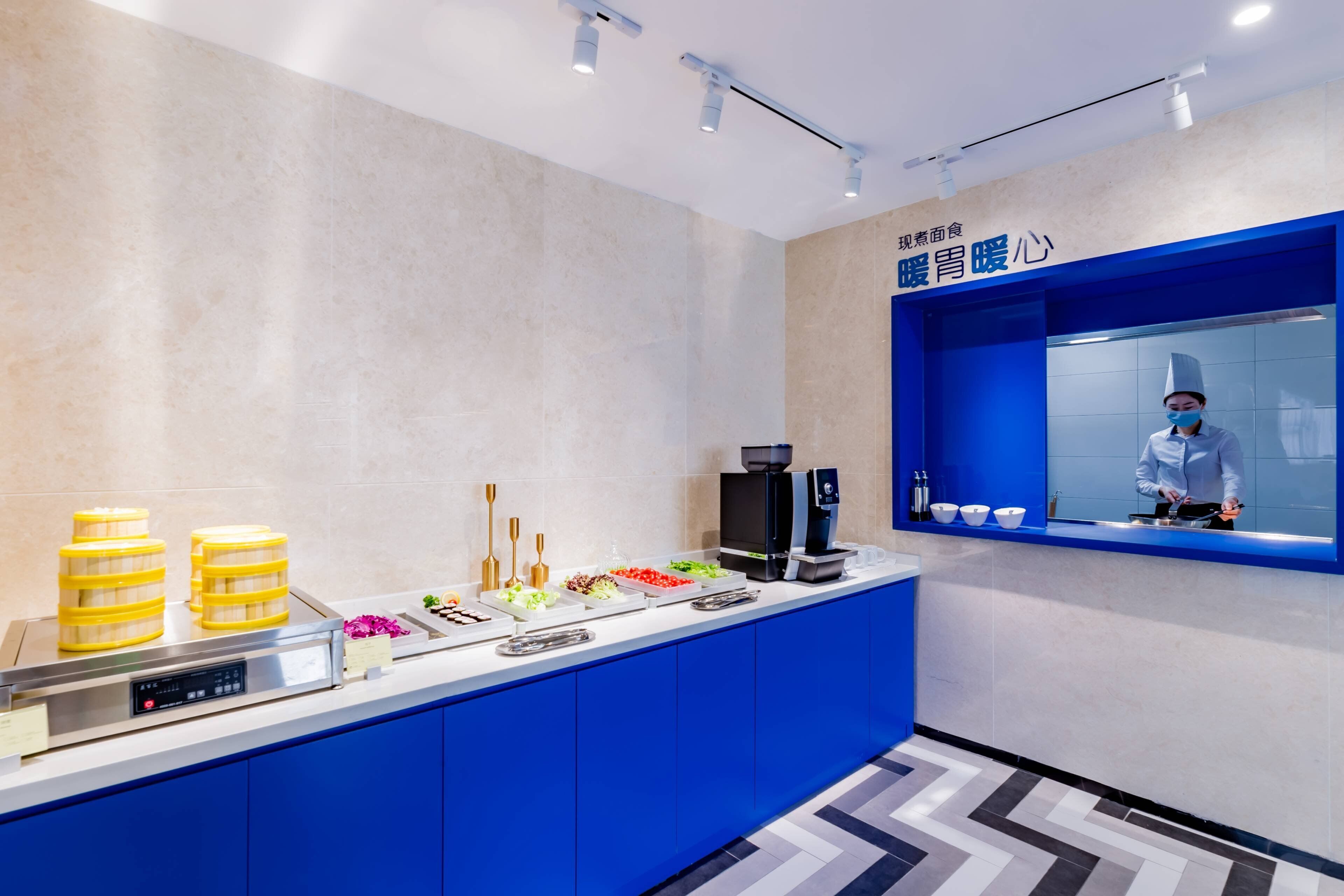 Un área de cocina moderna con una encimera azul, diversos alimentos, una máquina de café y una persona con uniforme de chef.