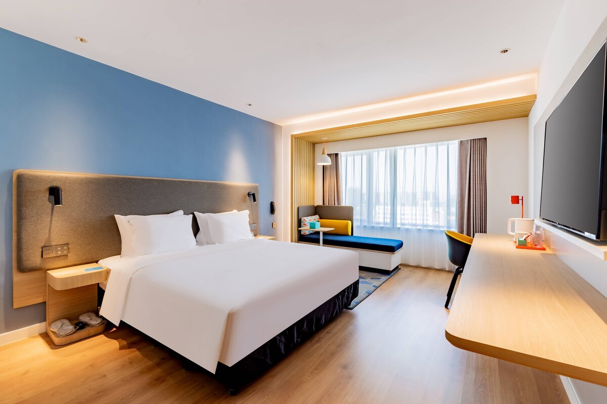A modern hotel room with a large bed, bedside table, and a TV.