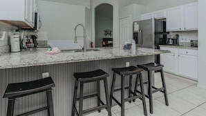 A kitchen with a large island, white cabinets, a stainless steel refrigerator, and a coffee maker.