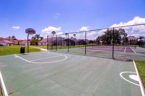 Un terrain de basket-ball en plein air, entouré d’une clôture, avec un panier de basket et une poubelle.