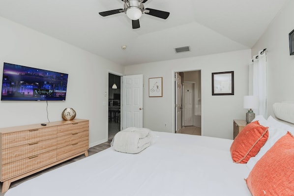 Un dormitorio con cama, ventilador de techo, televisor, cómoda y puerta que da a otra habitación.