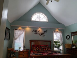 A bedroom with a sloped ceiling, a skylight, a bed with a patterned quilt, a wooden nightstand, a dresser, and a wall-mounted deer head decoration. - A fun filled,family friendly, farmhouse home, rural,but close to all amenities (Killingly)