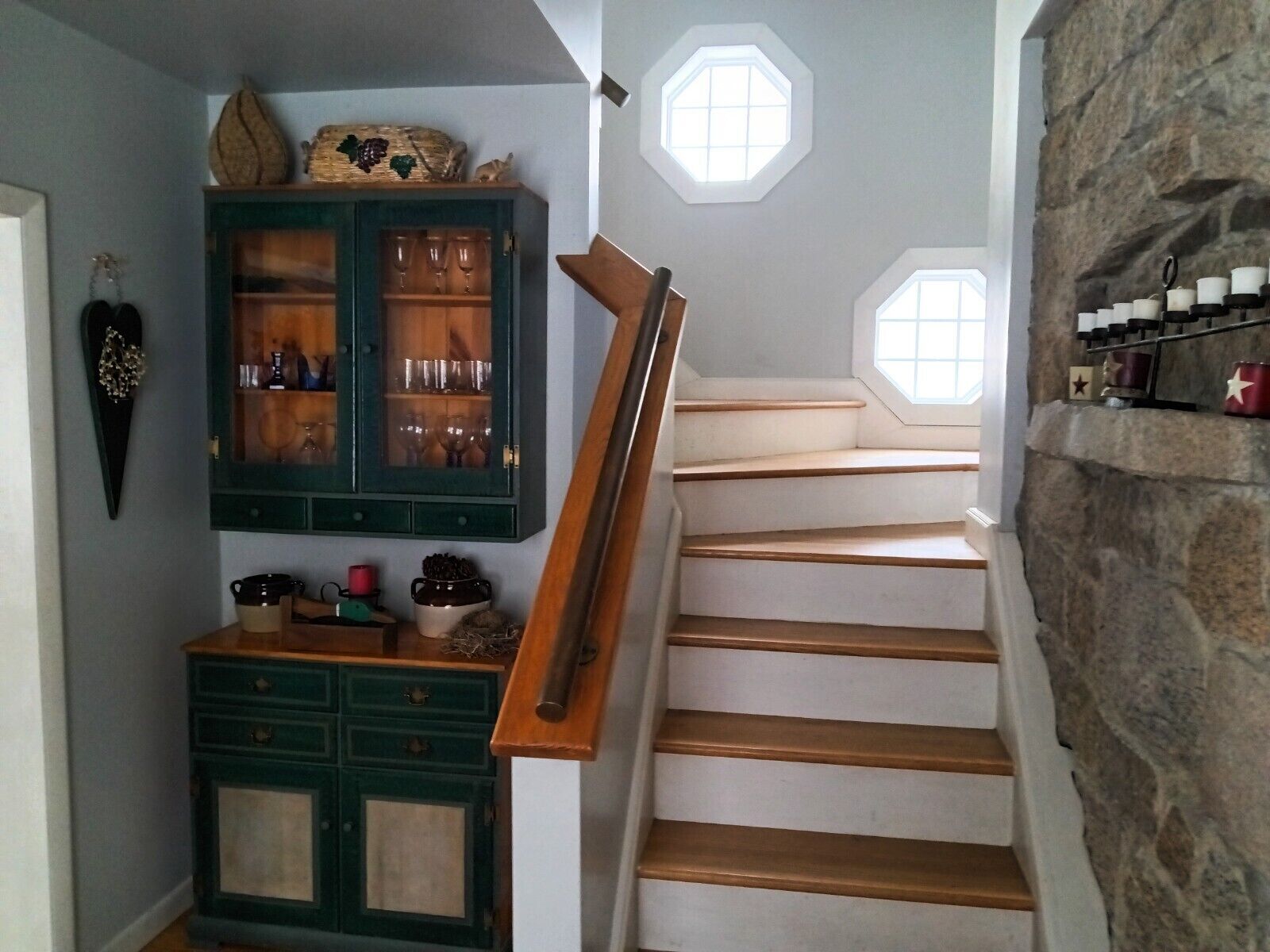 Una escalera de madera con peldaños y barandilla, que conduce a un rellano con un armario verde y una pared de piedra.