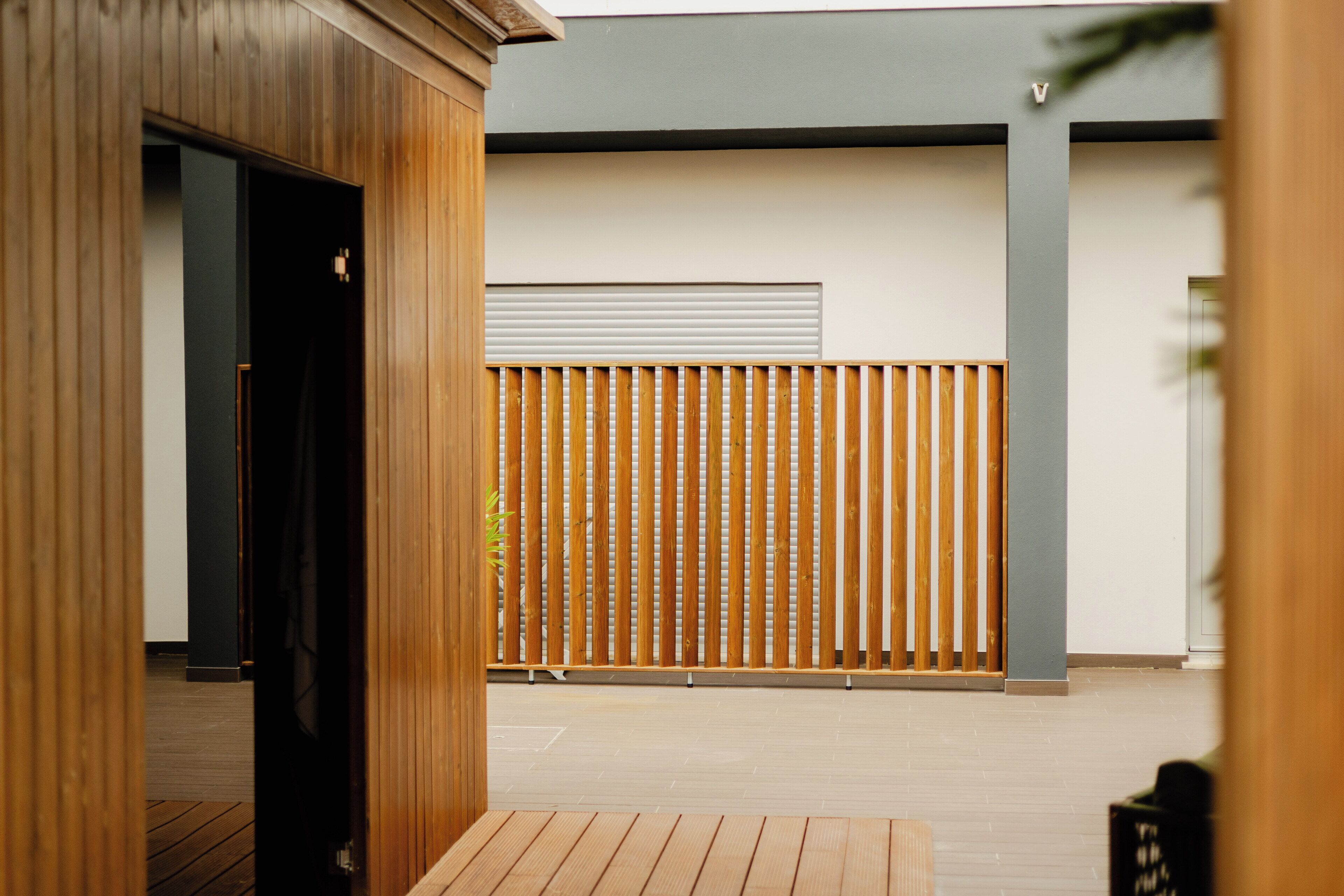 Eine Holzterrasse mit einer Schiebetür, ein senkrechter Holzzaun und ein modernes Gebäude mit einer grauen Fassade.