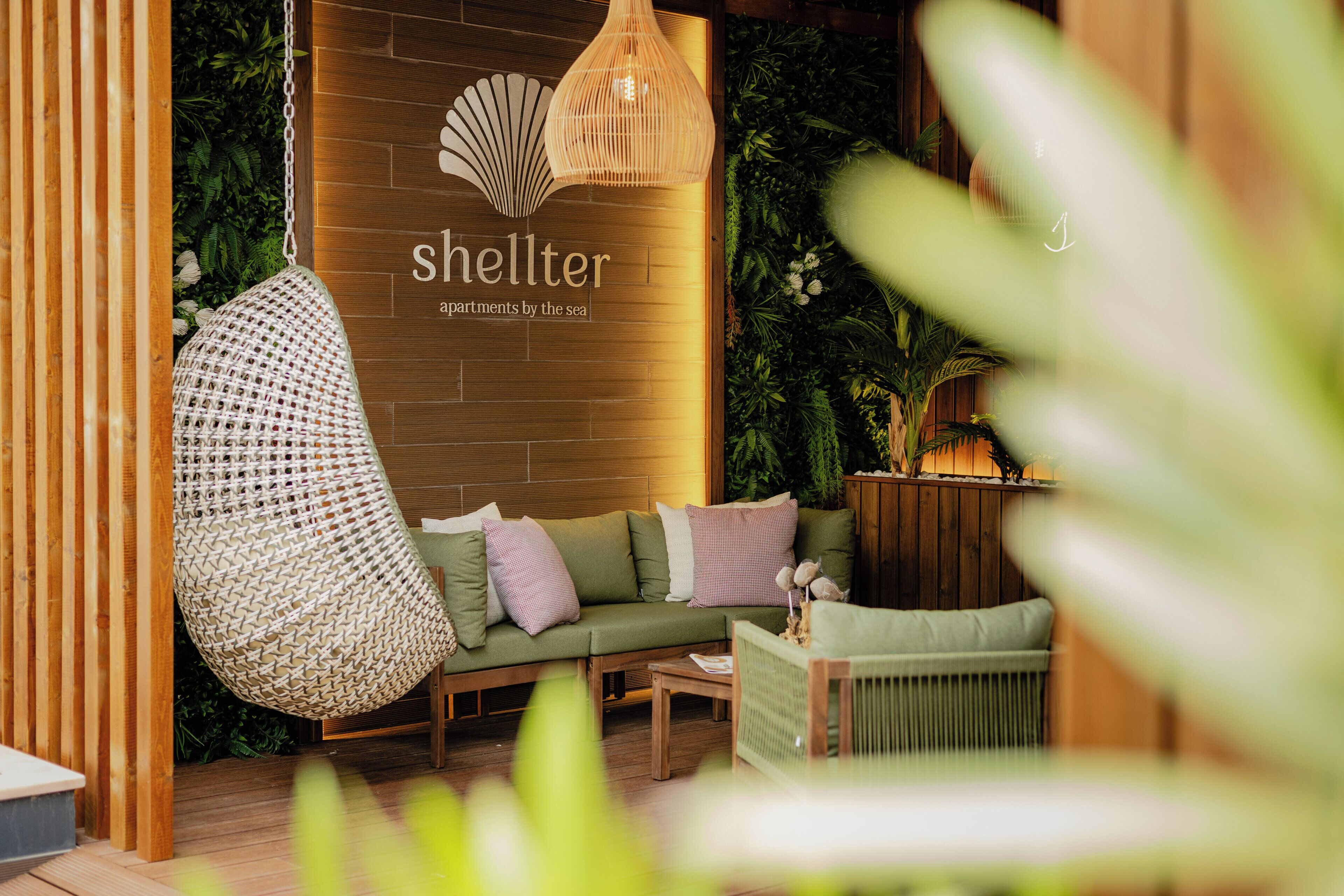 Un coin salon accueillant avec un fauteuil suspendu, un canapé et une petite table, le tout entouré de panneaux en bois et de plantes vertes.