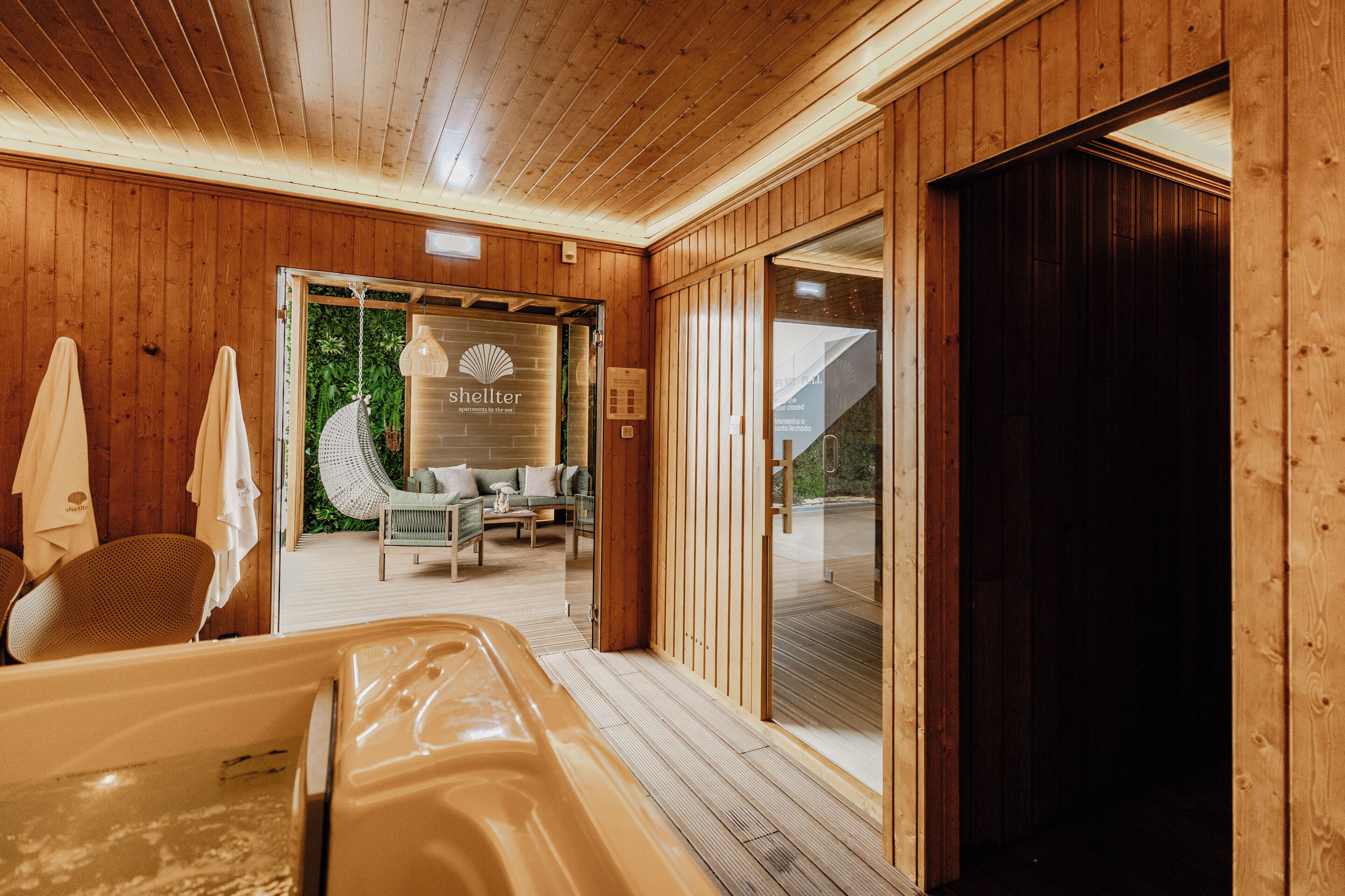Een houten interieur met een bubbelbad, een zithoek met uitzicht, en een glazen deur naar buiten.