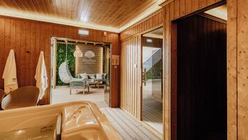 Een houten interieur met een bubbelbad, een zithoek met uitzicht, en een glazen deur naar buiten.
