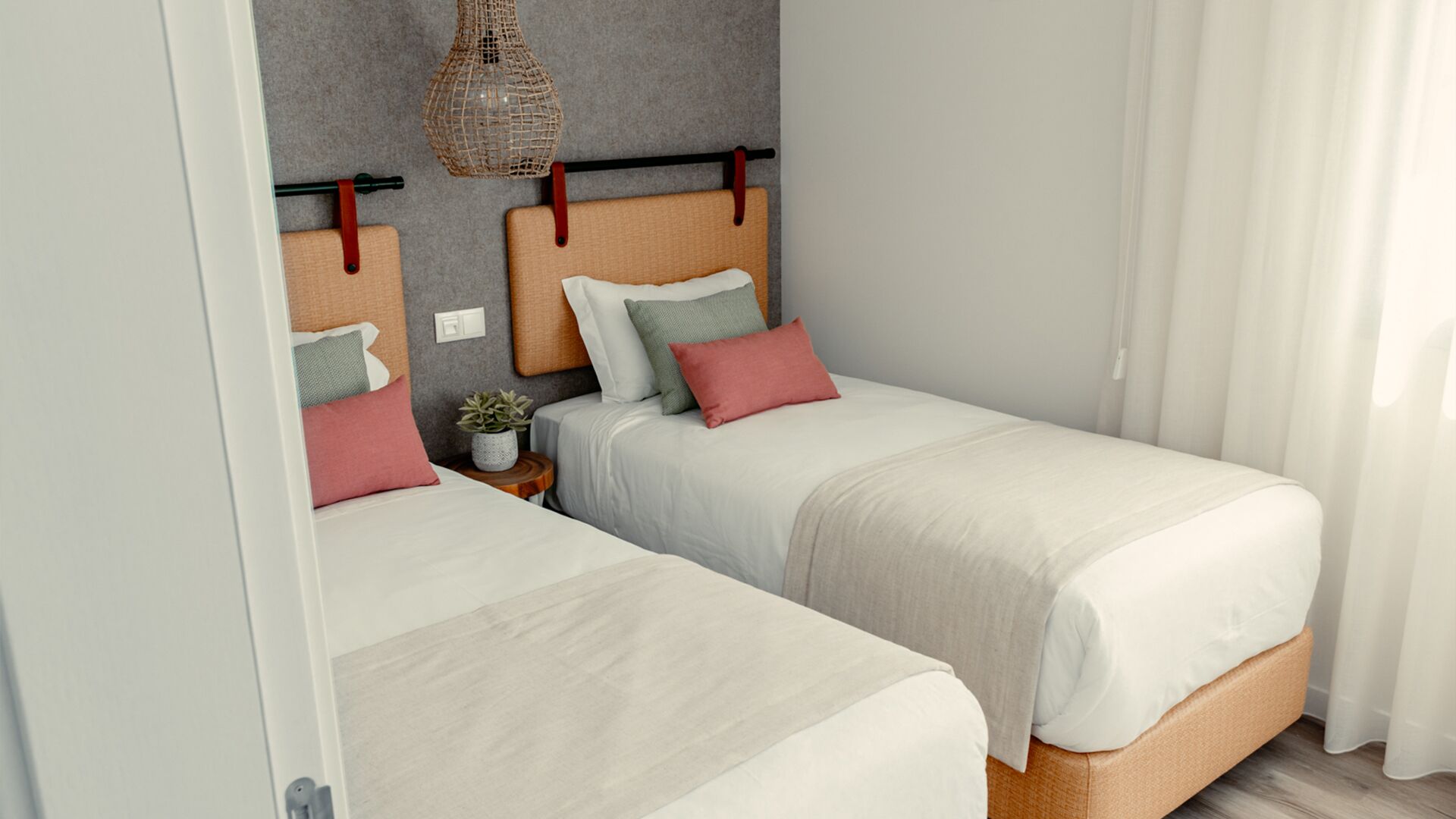 Habitación con cama doble, cabecera gris, mesita de noche con una planta y lámpara colgante.