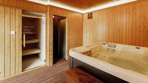 Uma sala de sauna de madeira com uma banheira de hidromassagem, uma porta com placa indicando abertura e fechamento, e piso de madeira.