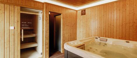 A wooden sauna room with a hot tub, a door with a push-pull sign, and a wooden floor.