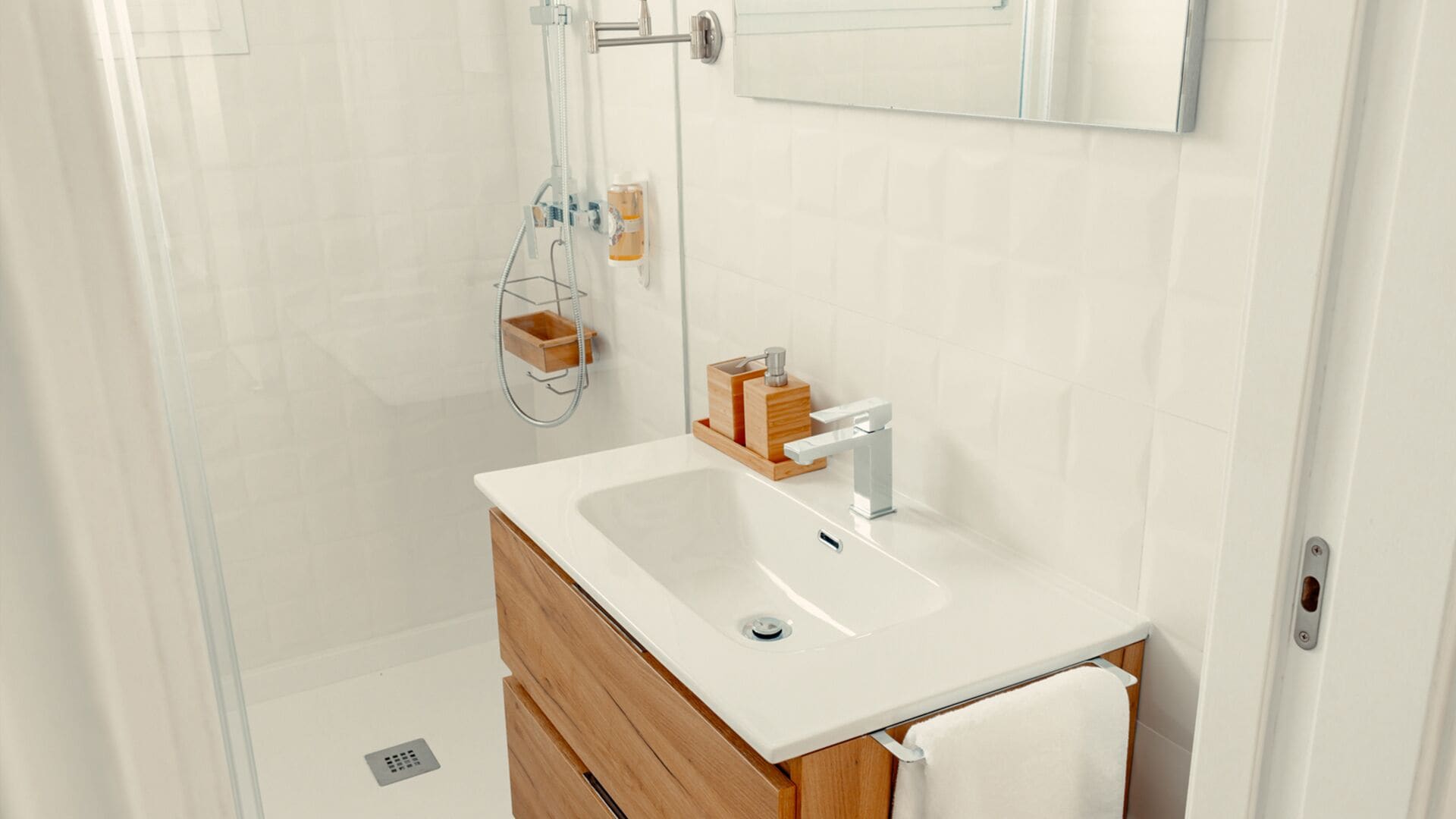 Un baño moderno con un lavamanos blanco, tocador de madera y cabina de ducha con paredes de vidrio.