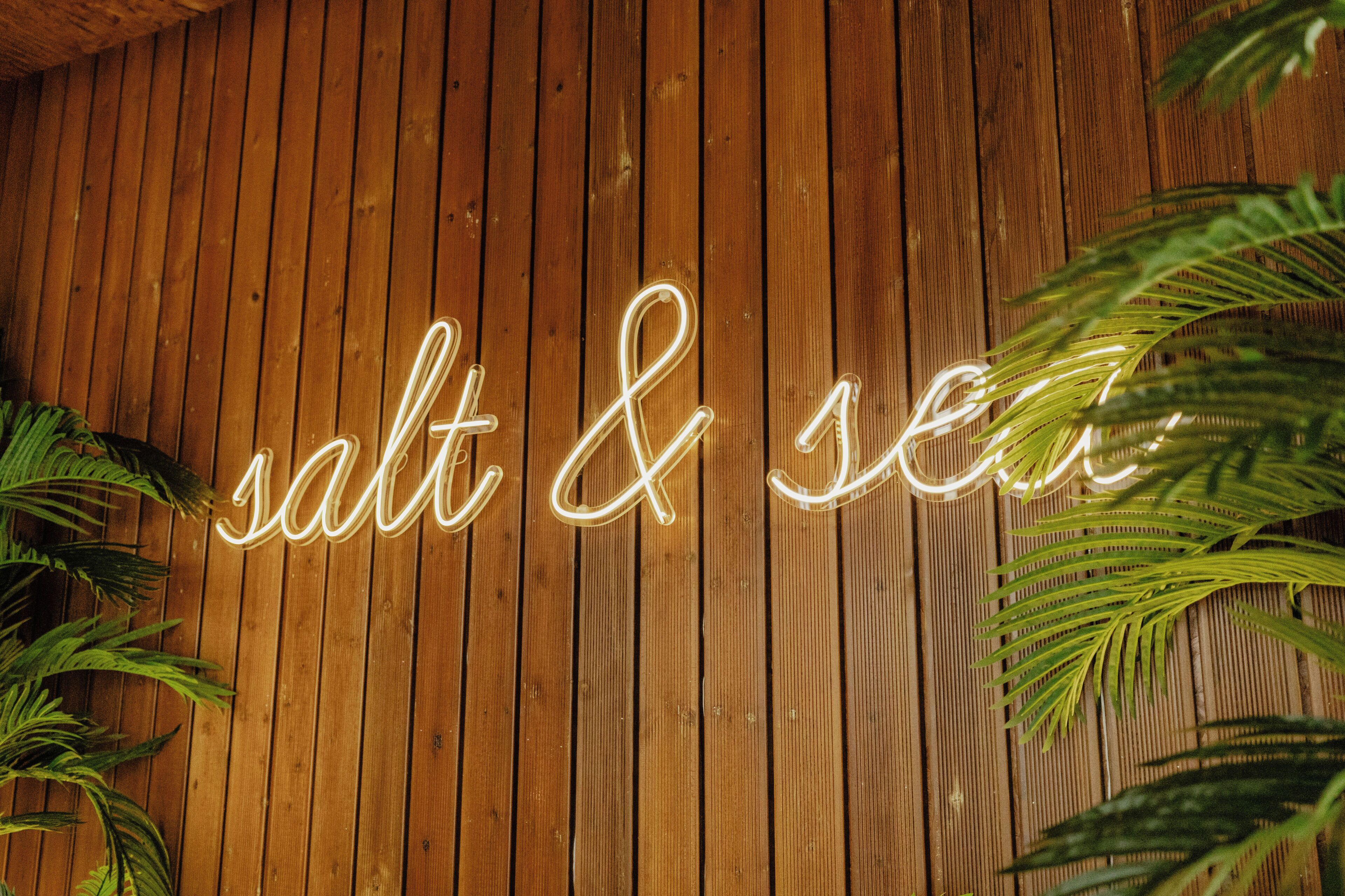 A wooden wall with a neon sign spelling 'salt & sea.'