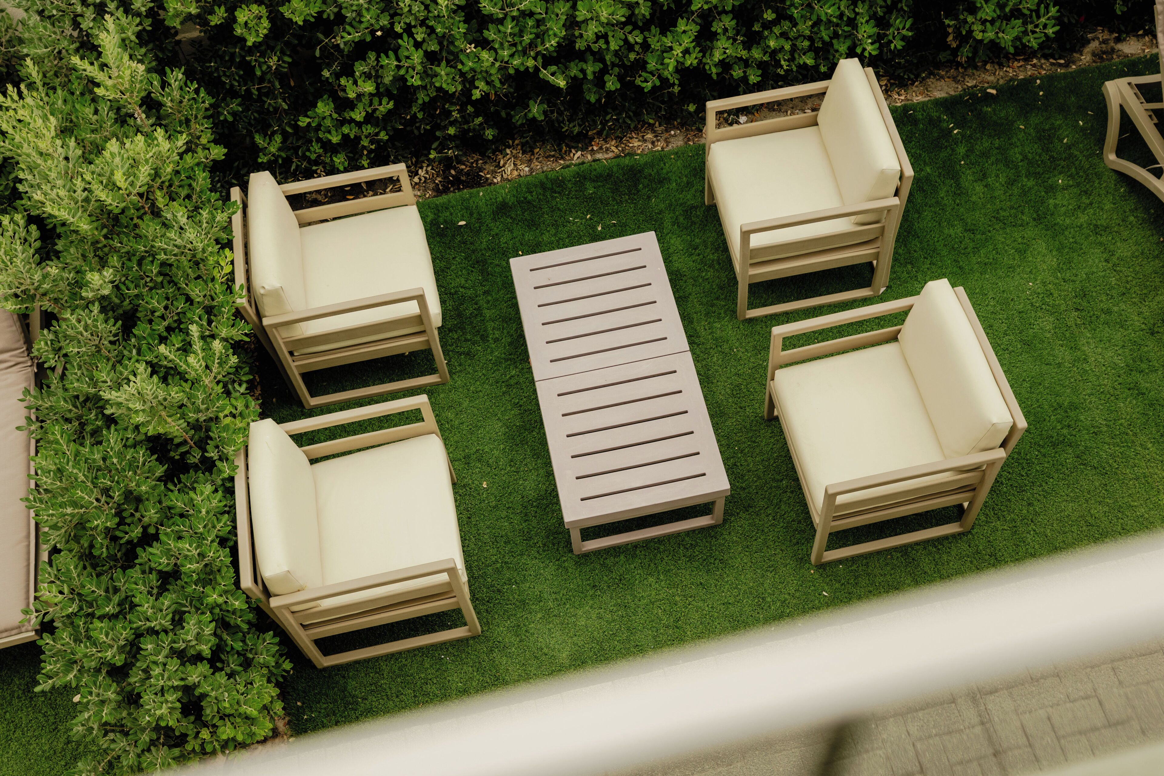 An outdoor seating area with four chairs and a table on a grassy lawn, surrounded by dense foliage.