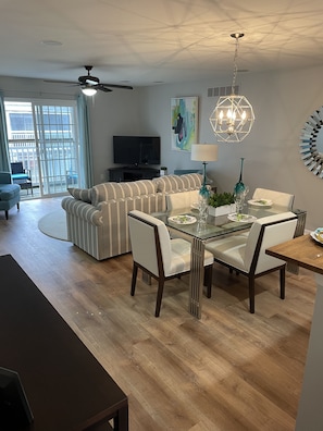 Un salon moderne avec un canapé, une table à manger et des chaises. On y trouve également un téléviseur et un ventilateur de plafond.