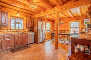 A log cabin kitchen with wooden cabinets, a stainless steel refrigerator, and a dining area with a wooden table and chairs.