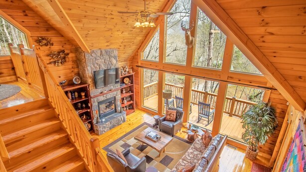 Une cabane spacieuse avec un intérieur en bois, une cheminée en pierre, une grande fenêtre et un escalier.
