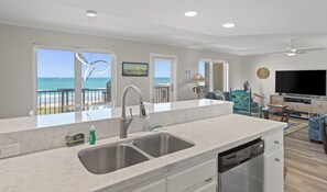 A modern kitchen with a large island, a dishwasher, and a view of the ocean.