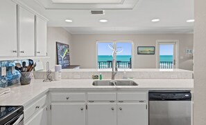 A kitchen with white cabinets, a stainless steel dishwasher, and a view of the ocean through a window.