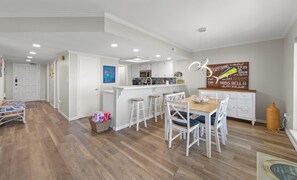 A modern kitchen with white cabinets, a central island with stools, and a decorative sign.
