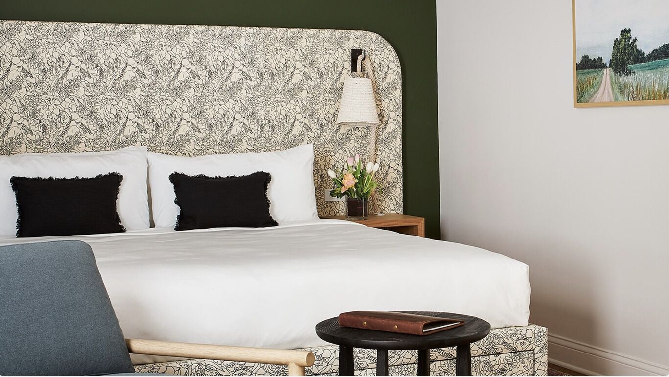 Una cama bien hecha con ropa de cama blanca y negra, una mesita de noche pequeña con una lámpara y un cuadro en la pared.