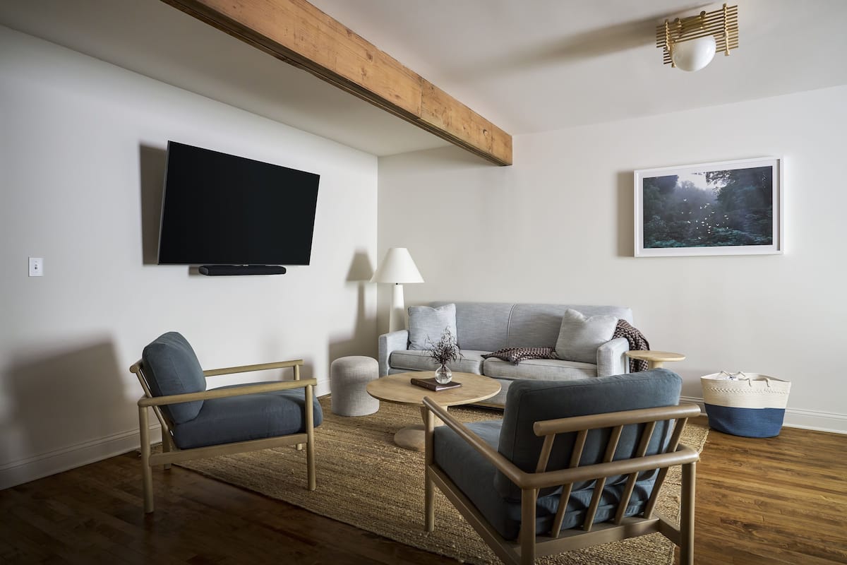 A modern living room with a flat-screen TV, a sofa, two armchairs, a coffee table, and a rug.