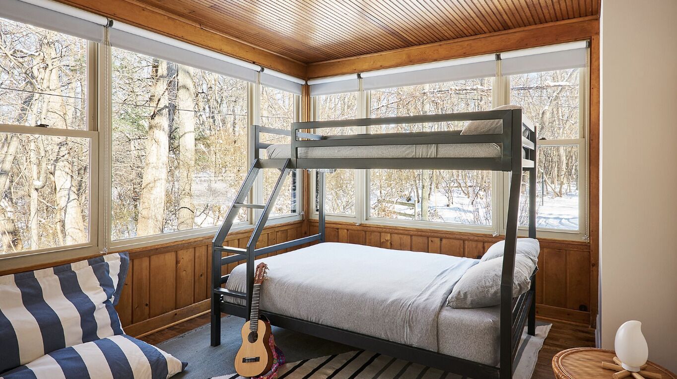 A bunk bed room with a window view of trees and a guitar on the floor.