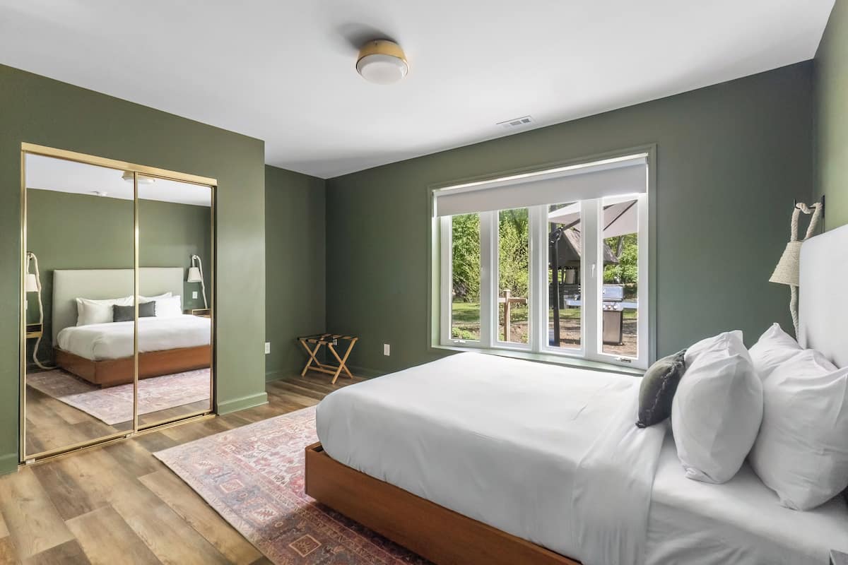 A bedroom with a large bed, a mirror, and a view of the outdoors.