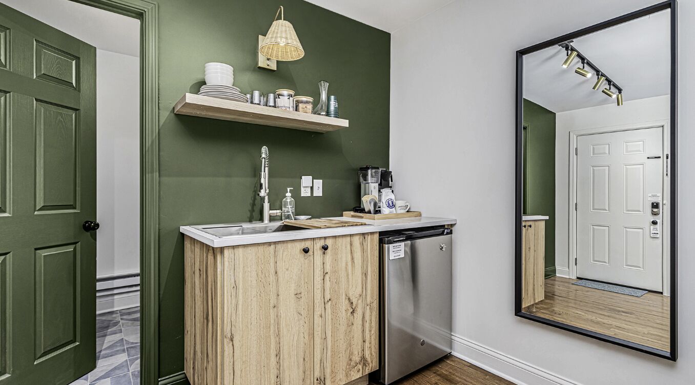 A kitchen with a wooden cabinet, a sink, and a dish rack. There is a mirror on the wall and a hanging light fixture.