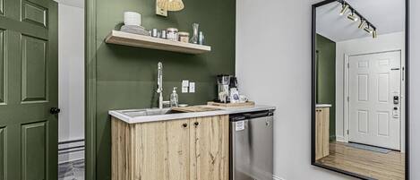 A kitchen with a wooden cabinet, a sink, and a dish rack. There is a mirror on the wall and a hanging light fixture.