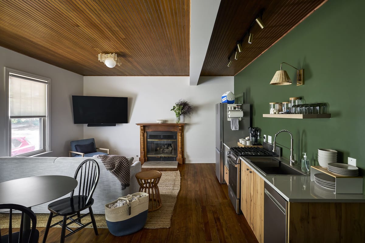 A modern kitchen with a wooden ceiling, a flat-screen TV mounted on the wall, and a built-in stove.