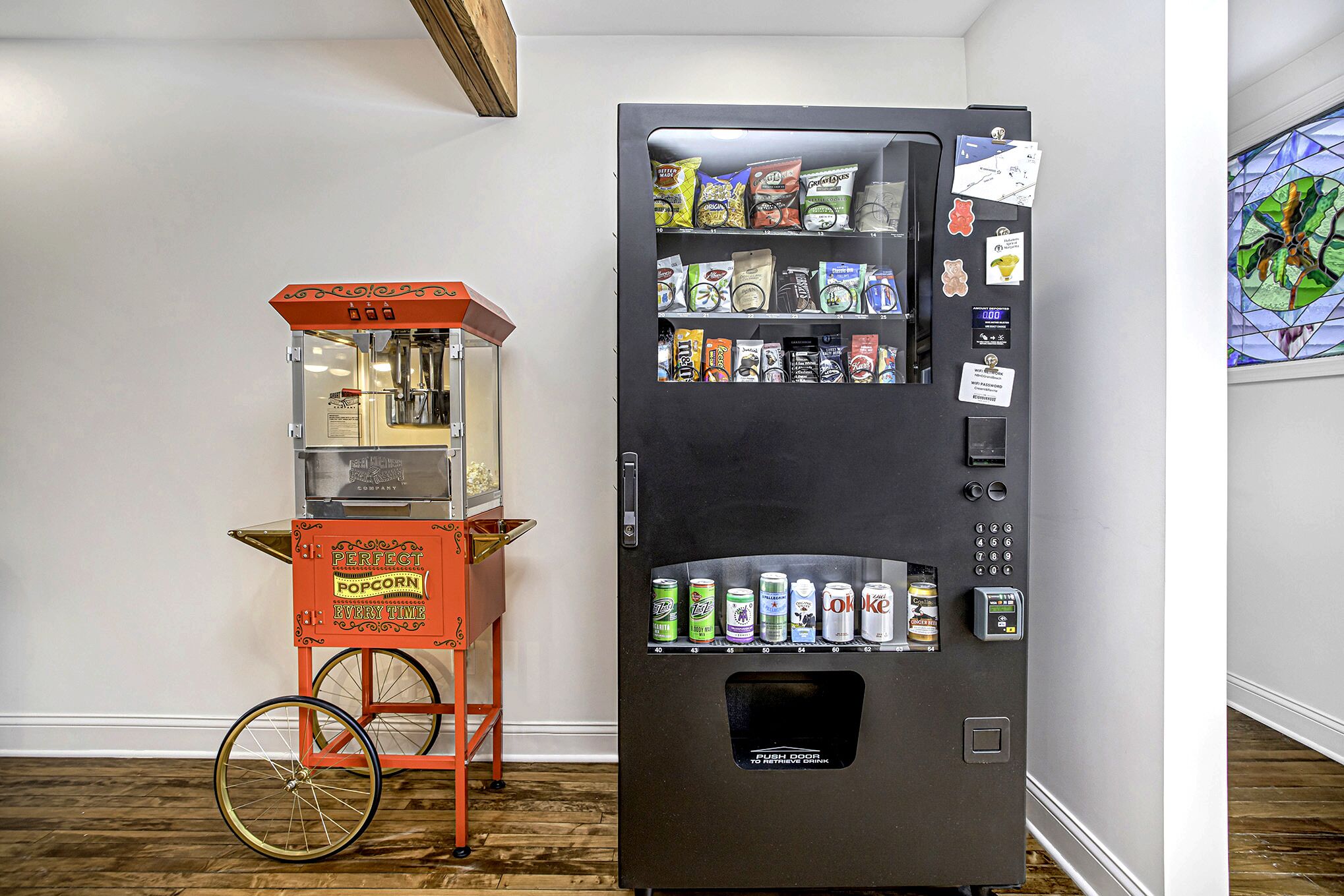 Une machine distributrice et un chariot à pop-corn se trouvent dans une pièce dont le sol est en bois et qui est ornée d’une fenêtre à vitraux.