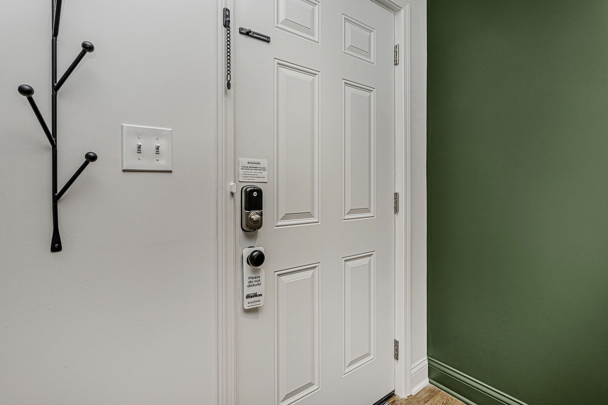 A white door with a keypad lock, a sign requesting not to disturb, and a wall-mounted light switch.