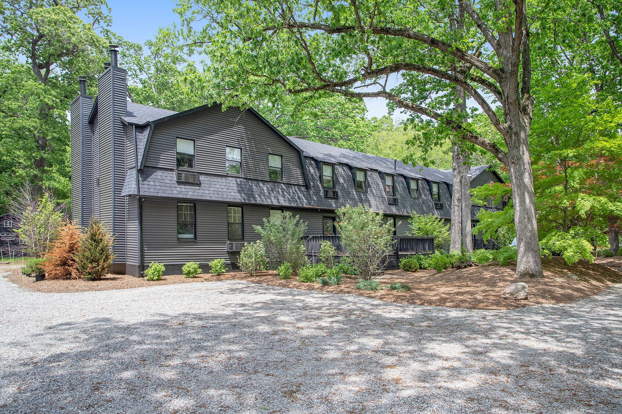 A two-story house with a sloped roof, multiple chimneys, and a gravel driveway.