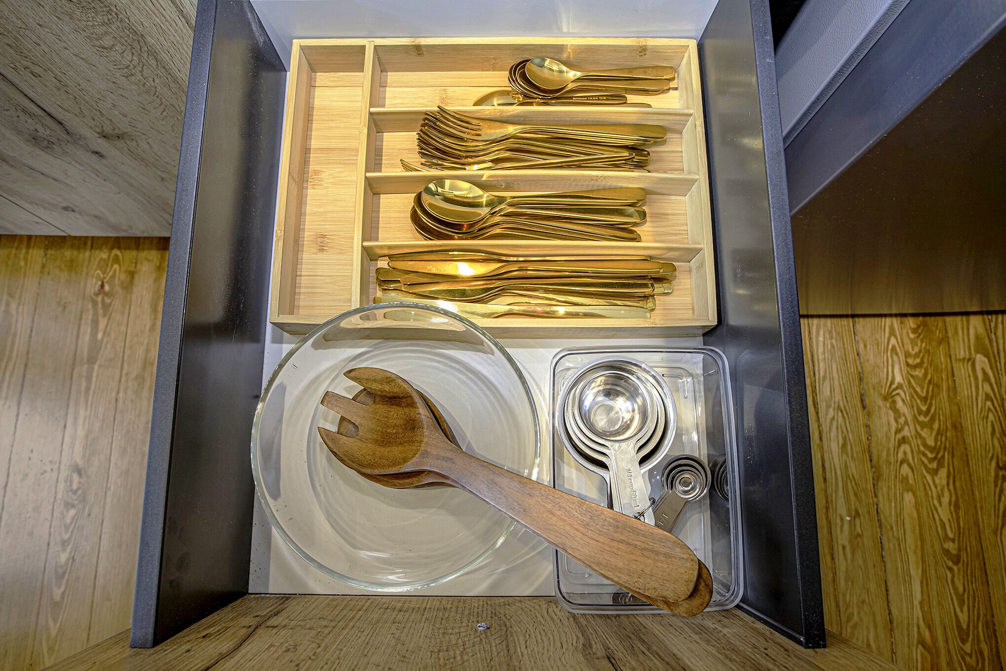 Un tiroir contenant des ustensiles de cuisine bien rangés, notamment des cuillères, des fourchettes et une spatule en bois.
