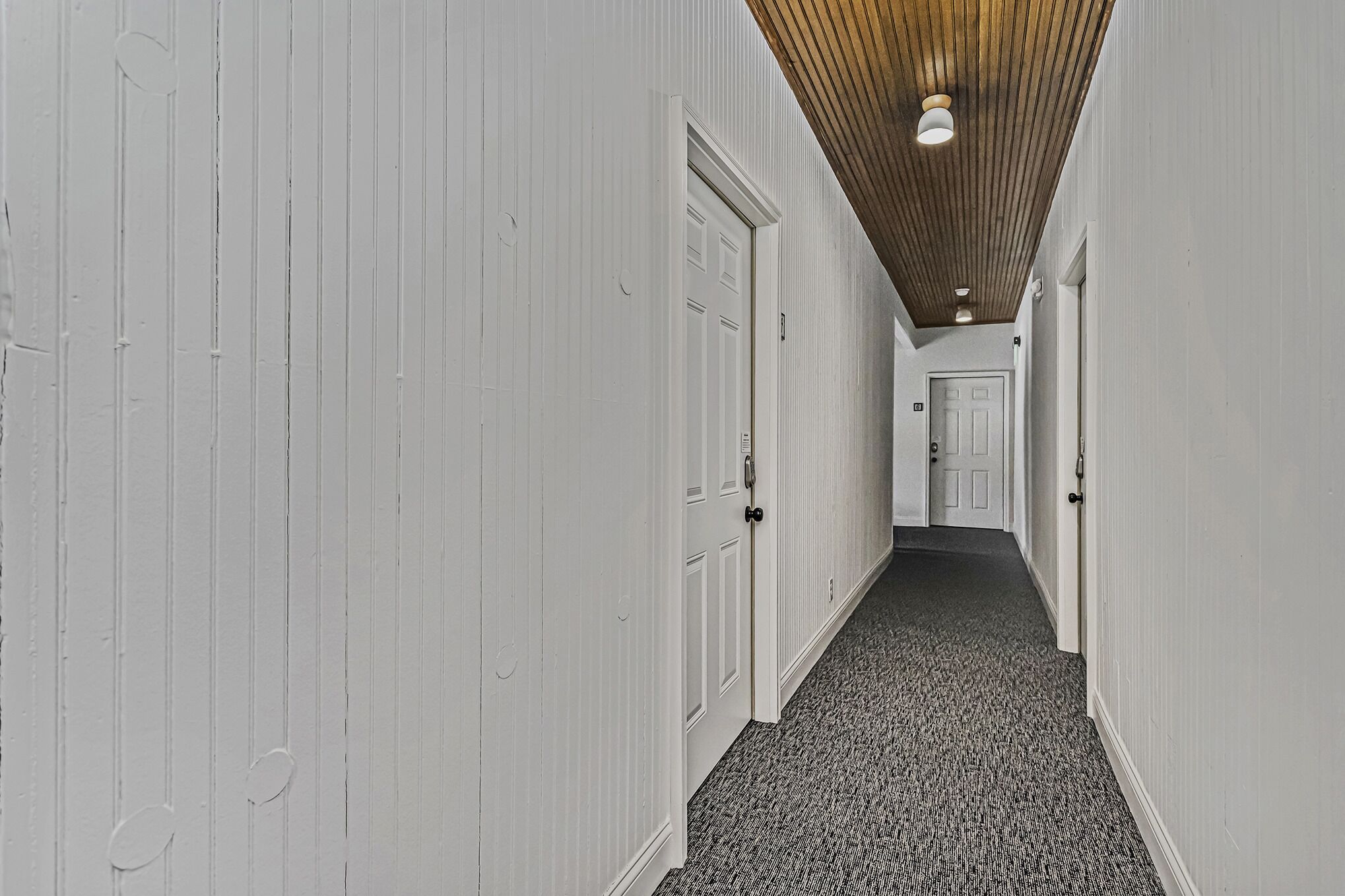 A narrow hallway with white walls and a patterned carpet.