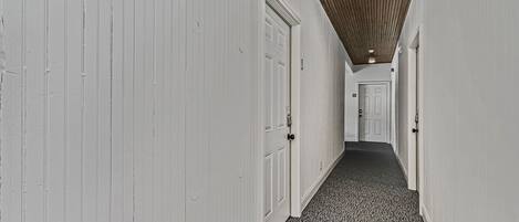 A narrow hallway with white walls and a patterned carpet.