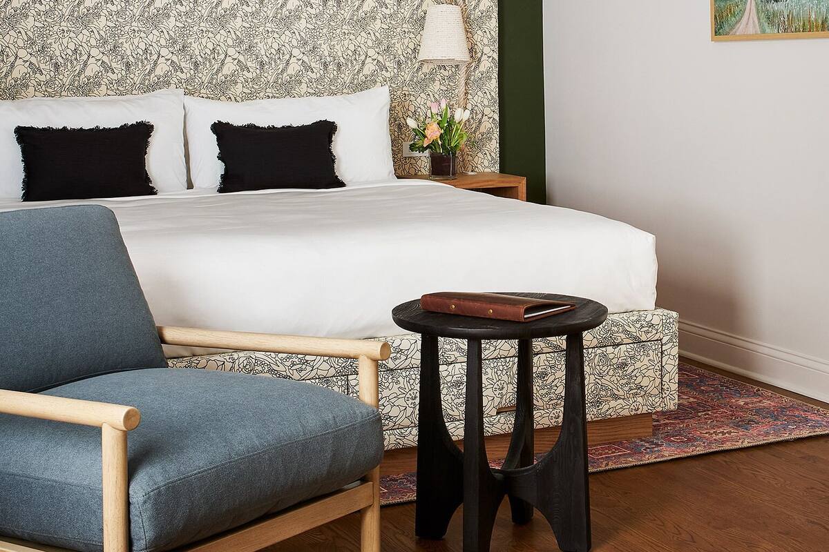 A bedroom with a large bed, a bedside table, a chair, and a painting on the wall.