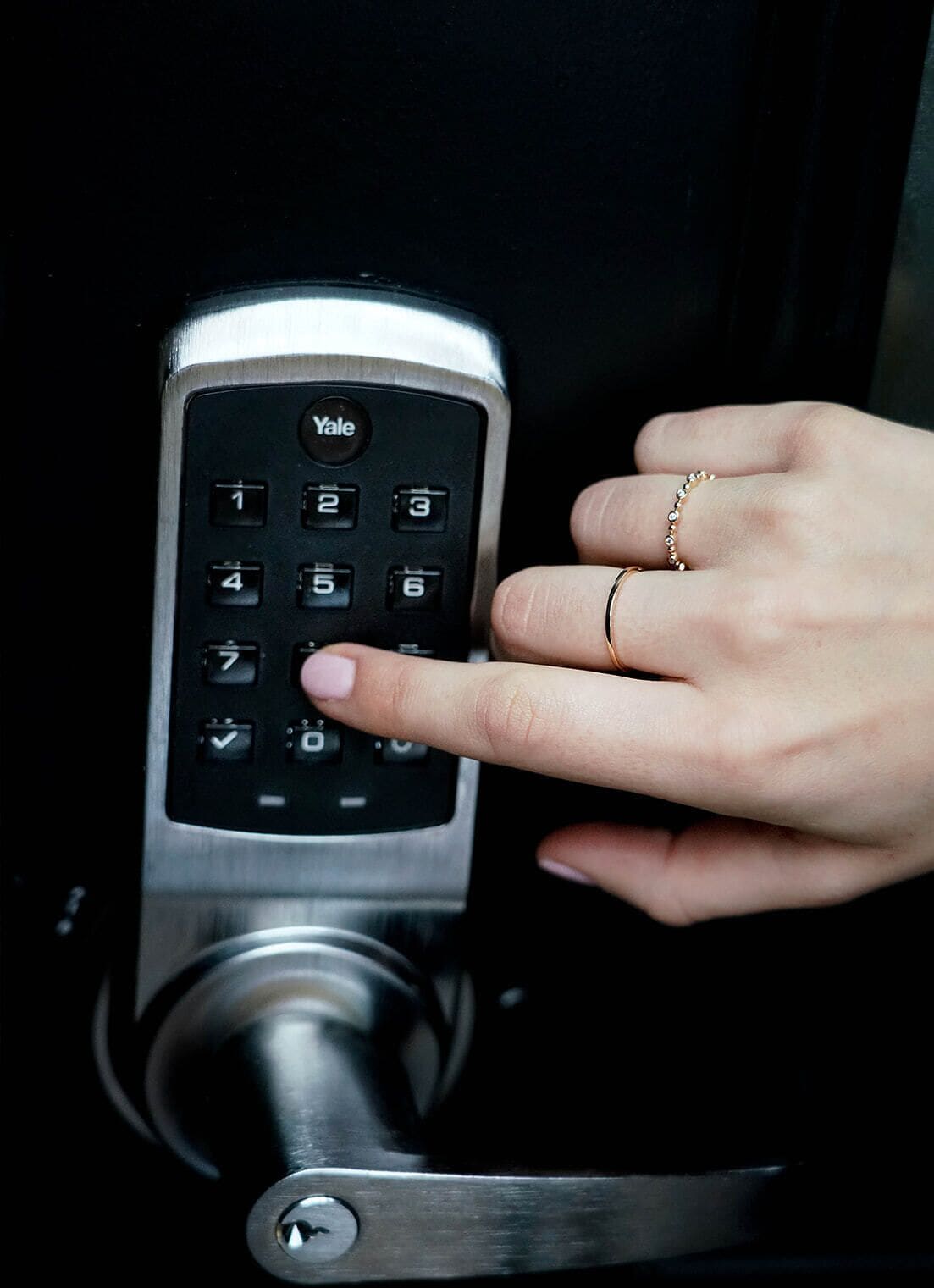 A hand pressing a keypad on a door lock.