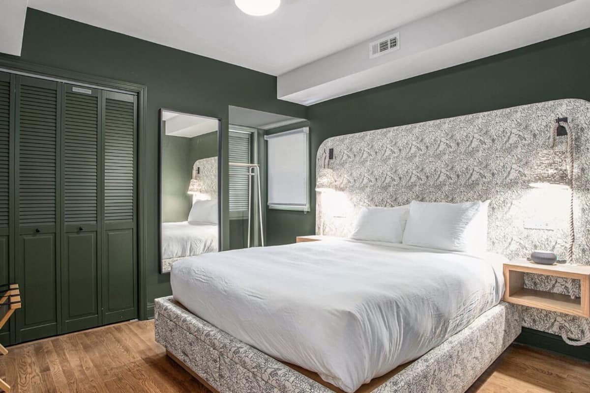 A bedroom with a large bed, green walls, a wooden floor, and a wardrobe with sliding doors.