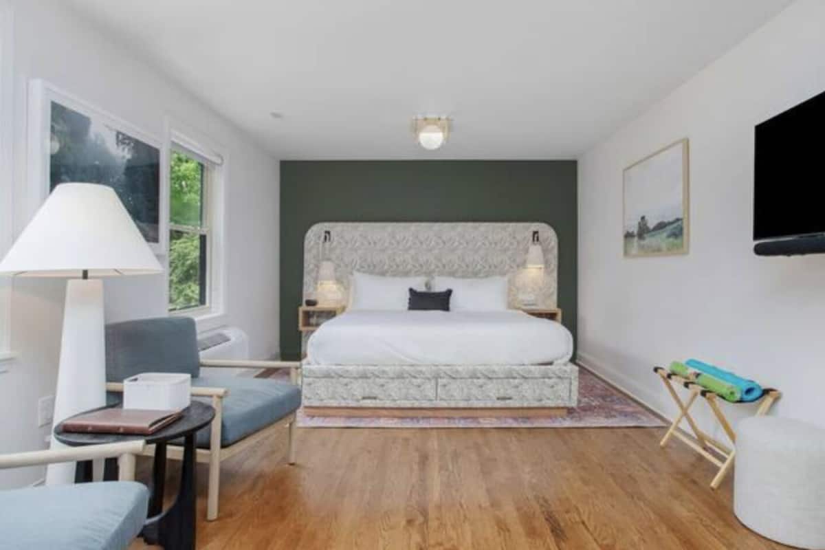 A bedroom with a bed, bedside lamps, a chair, a table, a TV, and a window.