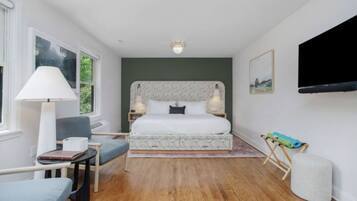 A bedroom with a bed, bedside lamps, a chair, a table, a TV, and a window.