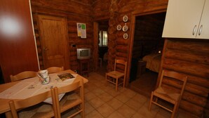 A cozy log cabin interior with a dining table, chairs, a television, and a kitchen area.