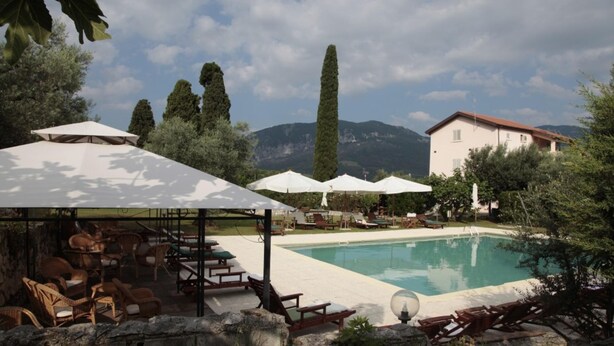 A pool area with lounge chairs and umbrellas, surrounded by trees and a mountain backdrop.