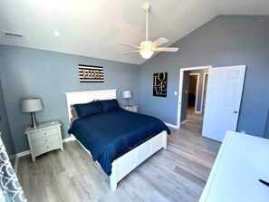Une chambre à coucher avec un lit, des tables de chevet, un ventilateur de plafond et une porte.