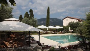 A pool area with lounge chairs and umbrellas, surrounded by trees and a mountain backdrop. - Chalet 6 Agriturismo (Tocco da Casauria)