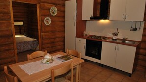 A cozy log cabin interior with a dining area, kitchen, and a small bedroom. - Chalet 6 Agriturismo (Tocco da Casauria)