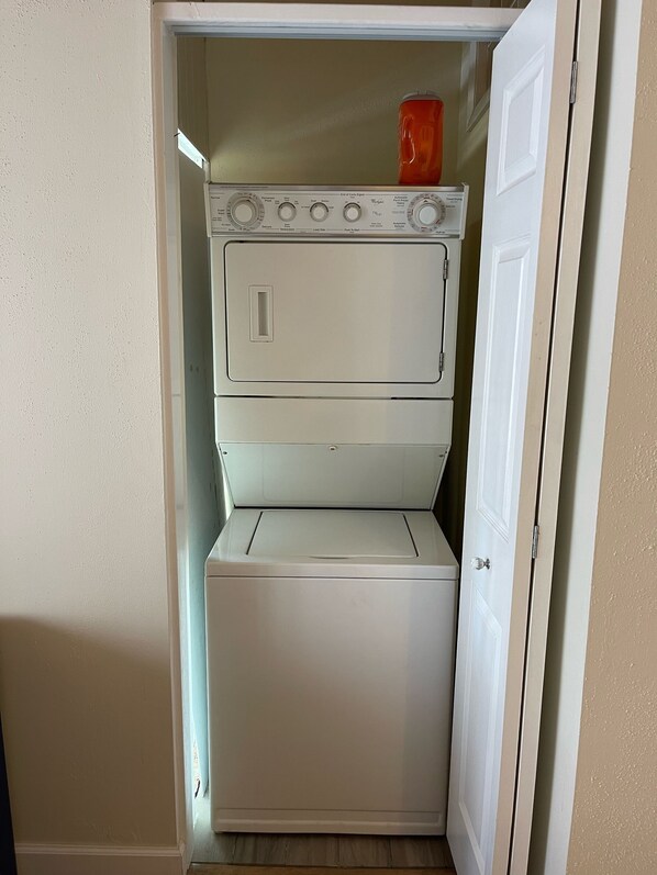 A compact, white laundry room with a built-in washer and dryer, a small shelf with a red container, and a white door. - Florida Keys Chic (Islamorada)